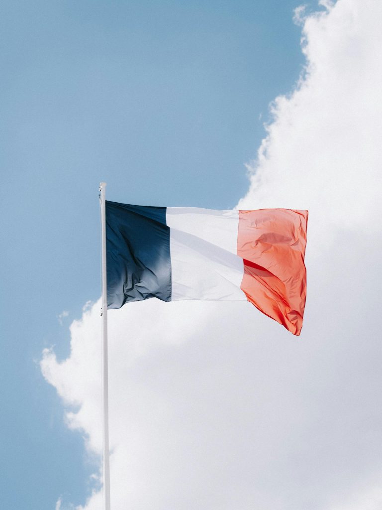 The French flag waving in the wind, set against a vibrant blue sky with clouds.